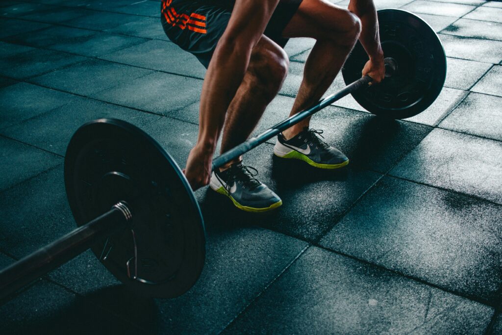 Close-up of a man in a gym preparing for a deadlift by squatting down and grasping a barbell with one plate on each side.