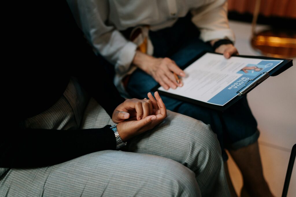  person holding a clipboard with a resume while another person sits nearby, hands clasped, appearing engaged in discussion—depicting an MBA admissions interview setting.