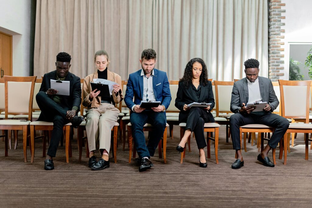 A gathering of individuals on chairs, discussing and reviewing papers in an interview setting.