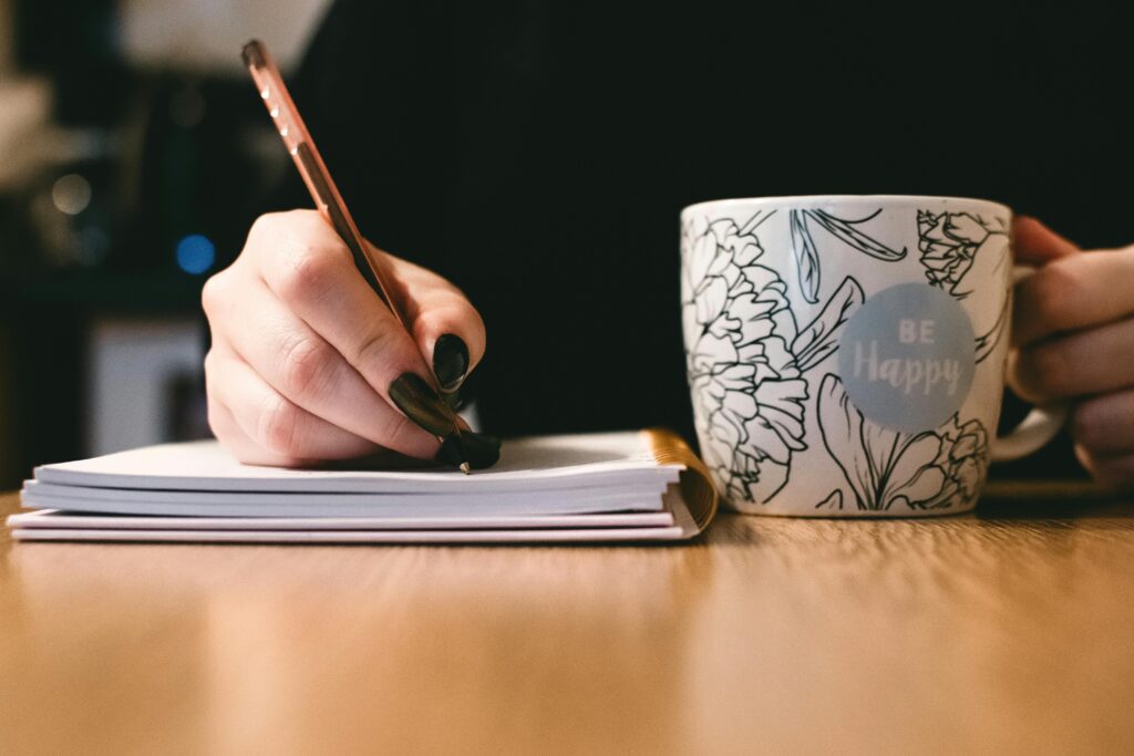 Person holding a white ceramic mug with "Be Happy" painted on it in black cursive text.